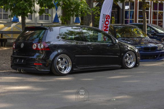 Schwarzer tiefergelegter VW Golf mit glänzenden Alufelgen auf einer Straße.