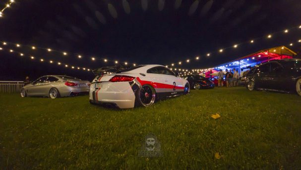 Zwei Autos auf einer Wiese nachts, umgeben von Lichtern und festlicher Dekoration.