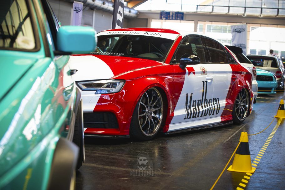 Roter Audi A3 mit auffälligem Design, in einer Werkstatt zwischen anderen Autos geparkt.